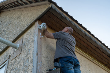 Adult male installing security camera on house exterior for home safety
