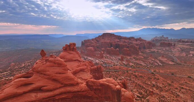 Orange rocks of whimsical shape in the deserted area. Beams of setting sun go through the cloudscape. Aerial perspective.