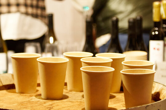 Group of disposable paper cups arranged on a wooden tray, surrounded by wine bottles, creating a casual and inviting atmosphere for gatherings
