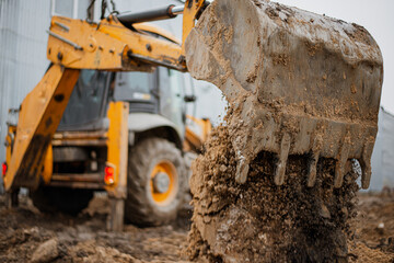 An excavator digs the ground for the foundation at the construction site. A yellow tractor pours earth out of the bucket. High quality photo © Rystemys