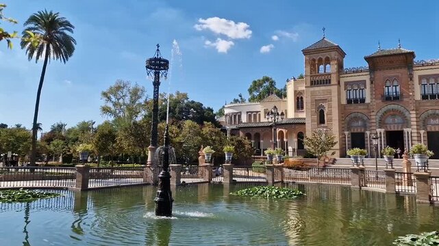 Historic Mudejar style building of Museum of Arts and Traditions of Seville reflected in peaceful pond with water lilies and iron lampposts in Maria Luisa Park Concept cultural heritage in Andalusia