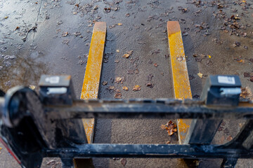 Yellow forklift forks on wet pavement representing logistics operation, construction handling, warehouse transport process and heavy equipment used for industrial load movement tasks