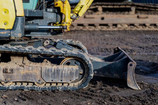 Tracked mini excavator on construction site showing rubber crawler system, hydraulic arm and metal bucket representing industrial machinery use, groundwork operation and excavation process