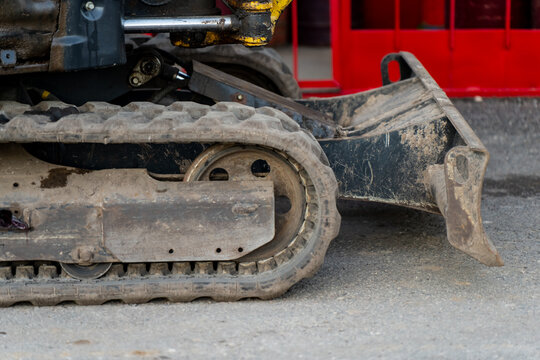 Industrial mini excavator undercarriage with rubber crawler track and steel dozer blade detail used for soil grading and earthmoving in construction site operations