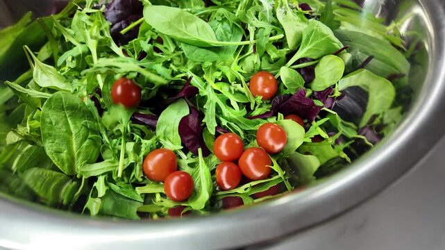 Bright colors of fresh greens and cherry tomatoes fill the bowl while ingredients are carefully mixed in a sunny kitchen. A healthy salad is being prepared with care.