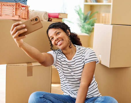 Portrait of a young woman girl unpacking boxes after moving in and relocation and making a selfie with a smartphone  in a new apartment, or packing to move out