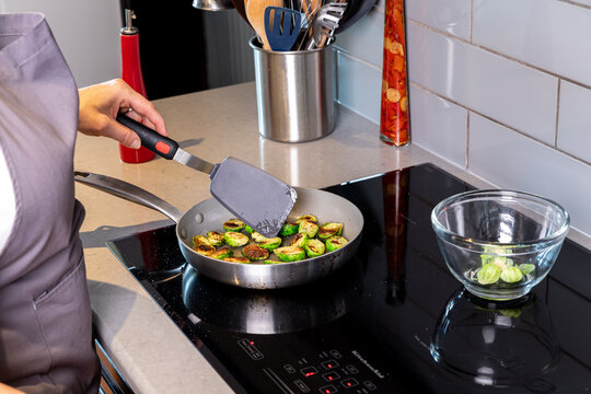 A woman frying brussels sprouts on an induction cooktop.