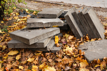 Stack of concrete slabs surrounded by fallen autumn leaves. Concept of construction, decay, and urban renewal in a seasonal outdoor environment