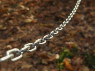 Close-up of a metal chain with shallow depth of field against blurred autumn leaves. Concept of connection, strength, or restriction in a natural outdoor setting