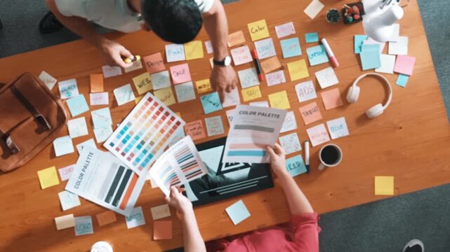 Top view of smart designer holding color palette while project manager looking at design and choosing color for program. Professional businesswoman taking a note while design creative logo. Symposium.