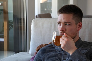 man drinking tea on couch while looking out of window at home