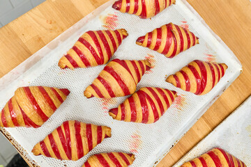 Freshly baked striped croissants arranged on a baking tray, showcasing golden pastry texture and vibrant red filling, perfect for culinary delights