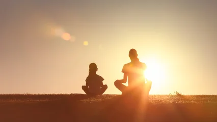 Fotobehang Rustgevend Silhouette of a mother and child meditating together outdoors at sunset, symbolizing peace, mindfulness, bonding, and healthy living  © kieferpix