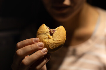 Close-up of a woman holding a bitten cookie, representing sweet cravings, snack food, dessert, and...