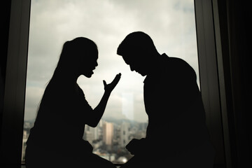 Silhouette of a couple arguing by a window, showing stress, frustration, and emotional conflict. Represents relationship problems, breakup, and communication issues