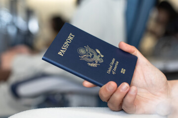 Close-up of a traveler holding a United States passport inside an airport. Represents travel,...