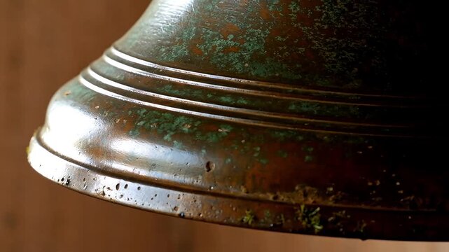 Close-up of an old bronze bell's flared lip showing green patina and verdigris over the dark metal surface with horizontal engraved lines