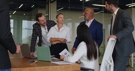 Business discussion of colleagues on office meeting, coworkers group standing at desk. Employees holding documents to discuss project, workflow of team planning, talking about analysis of chart report - Powered by Adobe