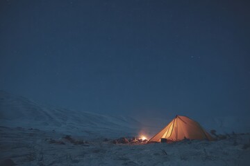 Glowing tent and fire on a snowy plateau under the starlit sky invite cozy winter adventures in the mountains