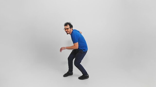 Man is sneaking tiptoeing and looking around with tricky smile on face filmed on white background. Isolated slow motion of young adult Caucasian person in casual clothes moving carefully like a thief.