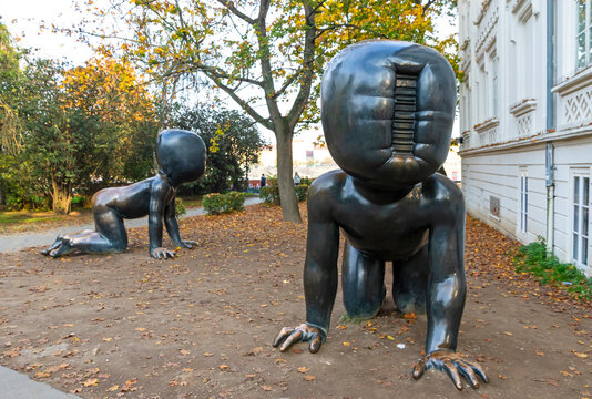 Crawling Babies sculptures (Czech: Miminka) by artist David Cerny at Kampa Museum. Faceless bronze toddlers with barcode faces crawl among autumn leaves