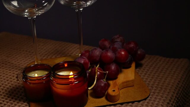 Still life two wine glasses with grapes bunch near romantic aroma burning flame fire candles on a table on dark backround. Decor concept of Christmas holiday celebration with fresh sweet ripe dessert