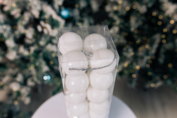 white Christmas balls in plastic packaging are lying on a table near a plastic Christmas tree in a...