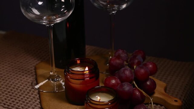 Still life two wine glasses with grapes bunch near romantic aroma burning flame fire candles on a table on dark backround. Decor concept of Christmas holiday celebration with fresh sweet ripe dessert