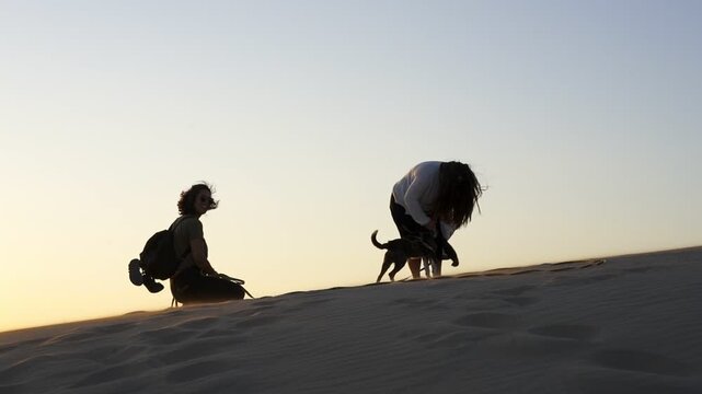 Silhouette of young women petting a dog on a sand dune in Patara beach in Turkey, in slow motion
