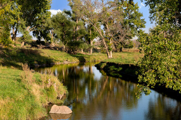 Winding creek and water reflection of trees in green pasture farmland of southwestern Minnesota © Kolanderverse