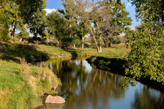 Winding creek and water reflection of trees in green pasture farmland of southwestern Minnesota