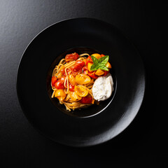 Top view of linguine pasta with cherry tomatoes and buffalo mozzarella on a black background