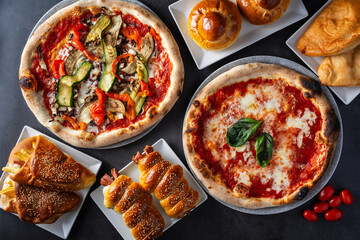 Top view of vegetable pizza and margherita pizza, plus other typical Italian baked goods on a dark background
