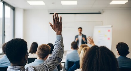 Close-up of a person's hand raised in the classroom, seeking attention from the speaker in front of a projector screen.