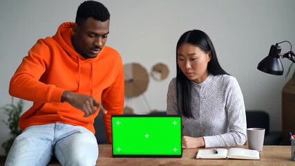 Diverse young colleagues collaborating on a project discussing ideas while looking at a tablet with a green screen for easy content insertion in a modern and bright office setting.