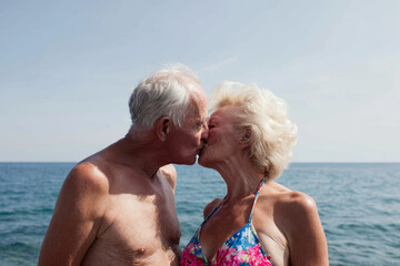 Elderly couple kissing at beach, showcasing love and affection against serene ocean backdrop. Their joyful expression highlights beautiful moment