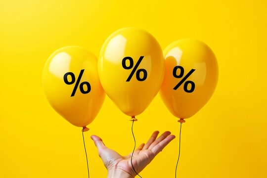 A hand holds three bright yellow balloons, each featuring a black percentage sign (%), against a vibrant yellow background  symbolizing discounts, promotions, or financial savings.
