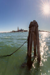 Fototapeta premium Wooden mooring post with chains in foreground and San Giorgio Maggiore island in background in Venice, Italy