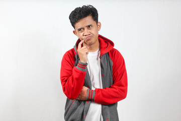 Asian man in a red and gray hoodie is captured in a moment of thoughtful consideration.