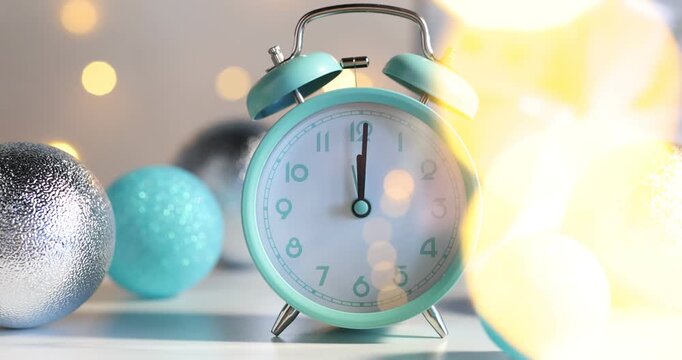 Alarm clock and baubles on light table against grey background with flashing blurred lights, closeup. Happy New Year