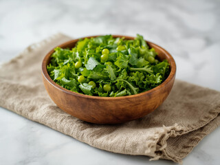 Wooden bowl filled with green salad of lettuce, peas and herbs on linen cloth over marble surface, side view in soft natural light for menu use.