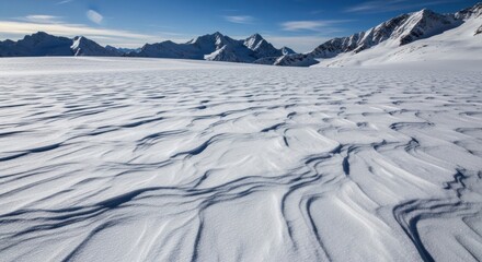 Majestic Winter Landscape: Wind-Sculpted Snow Patterns Lead to Towering Snow-Capped Mountains Under a Bright Blue Sky