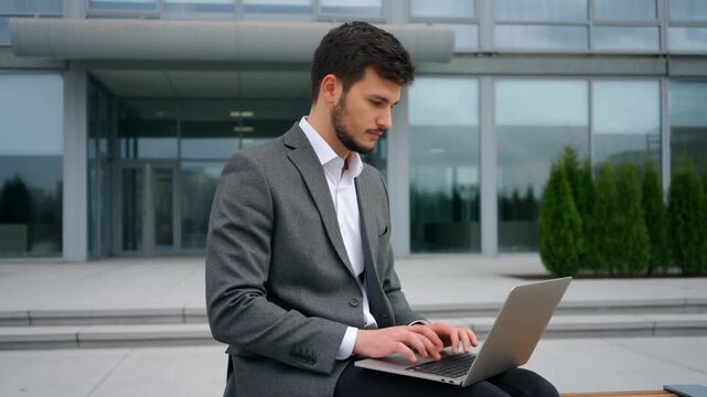 A focused businessman using laptop outside modern office building Stock Video