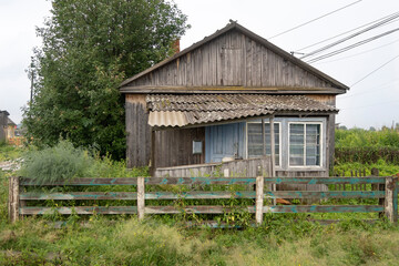 Obraz premium A countryside street with an old wooden house with a leaning canopy among tall grass bushes