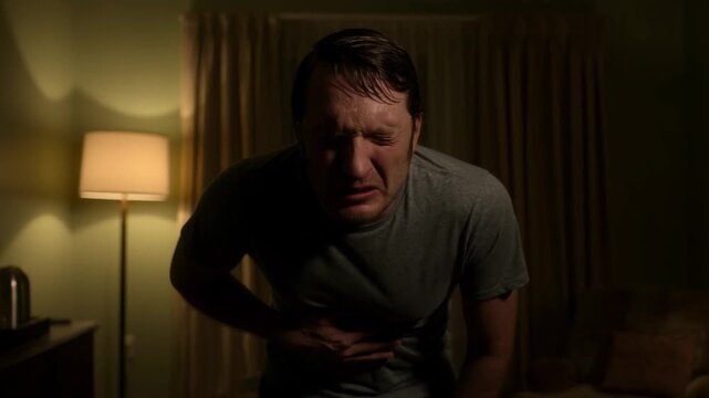 A man is suffering from stomach pain, hunched over, and clutching his abdomen Stock Video