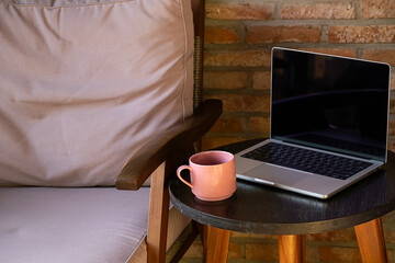 Laptop and drink mug on round table, next to an armchair