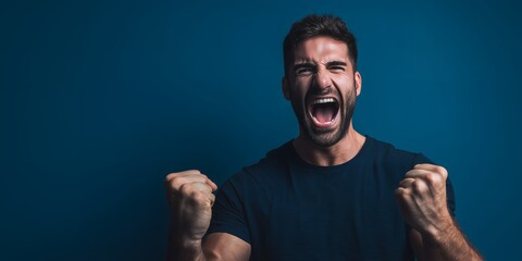 Man shouting with clenched fists against a dark blue background expressing strong emotion, concept for achievement, success and winning a challenge