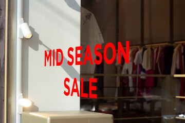 Horizontal photo. Red text Mid season sale. Sticker on glass showcase window of clothing store. Concept of 11 november, mega discount, online shopping, Black Friday, gift, offer, cyber monday, holiday