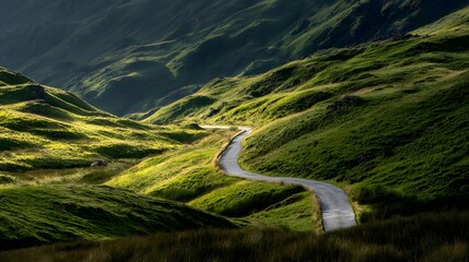 Winding asphalt road descends through rolling sunlit green mountain valley