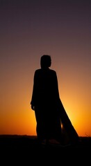 Fototapeta premium Solitary figure stands silhouetted against a dramatic desert sunset sky